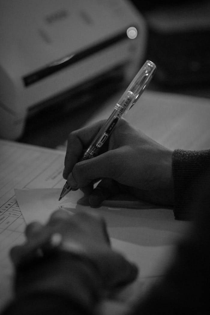 Black and white shot of hands writing with a pen on paper, conveying focus.
